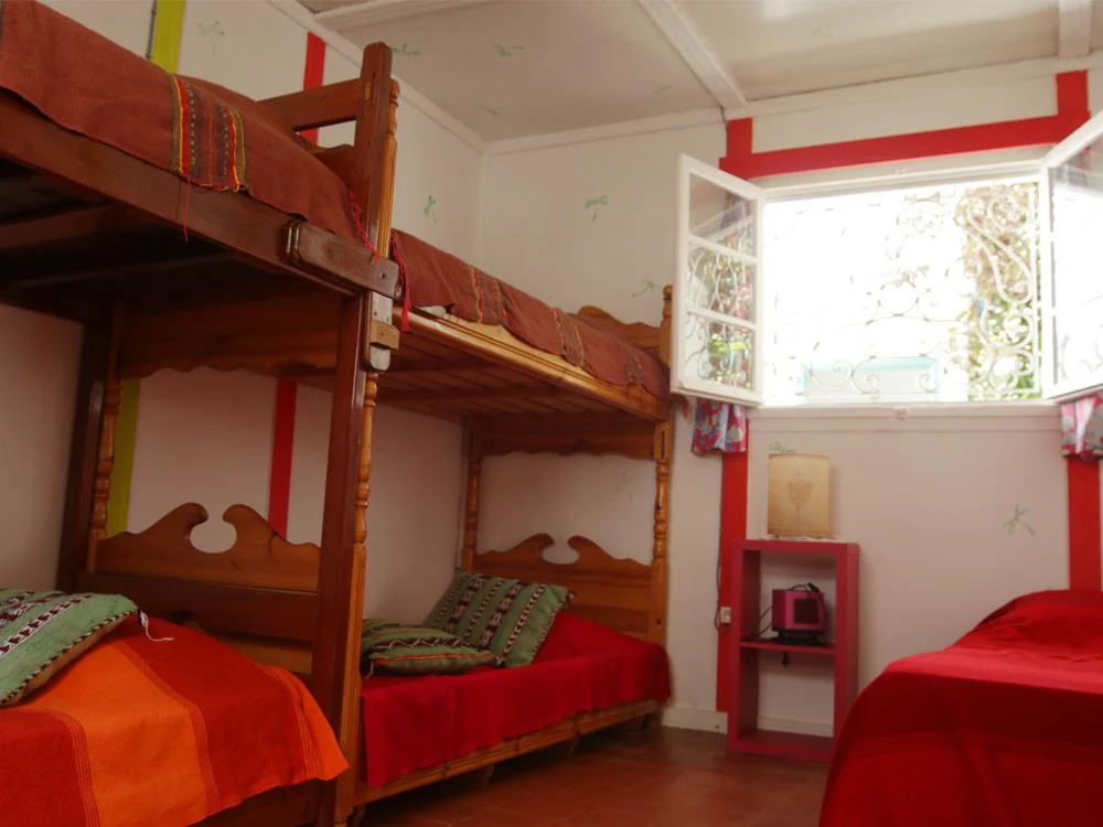 Rustic bunk beds with red and orange striped bedding in a red-trimmed white room, with an open window letting in light